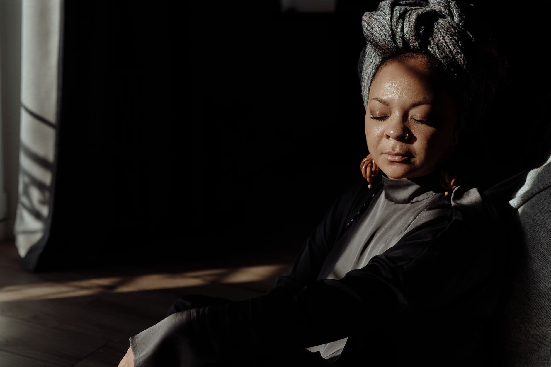 A Black woman resting peacefully with her eyes closed in warm light, reflecting the calm of mental wealth